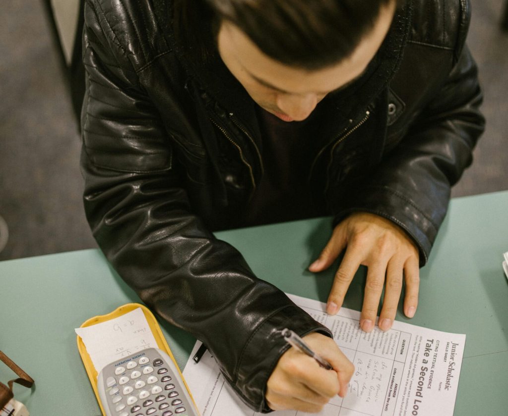pexels-photo-7092389-7092389 Student using calculator while taking an exam in a classroom setting, focusing on mathematical problems.